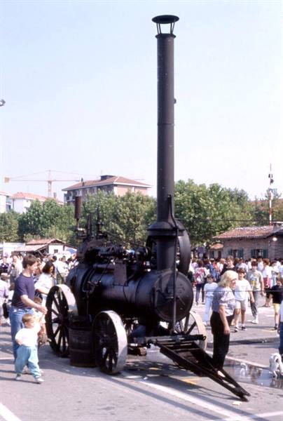 Black steam traction engine with tall chimney displayed at fair among crowd