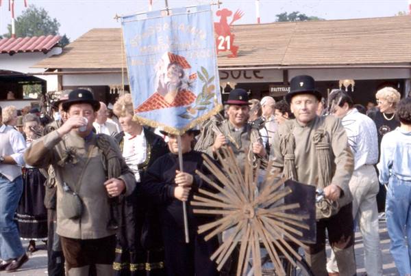 Men in traditional costume with banner and wooden wheel at village festival