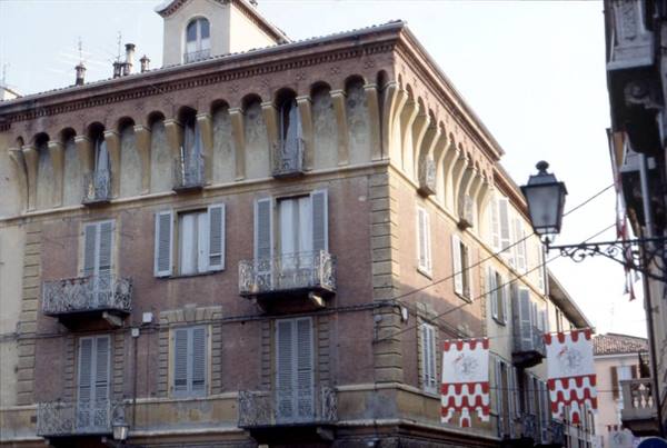 Stuccoed building with arched loggia and red-and-white banners on street corner