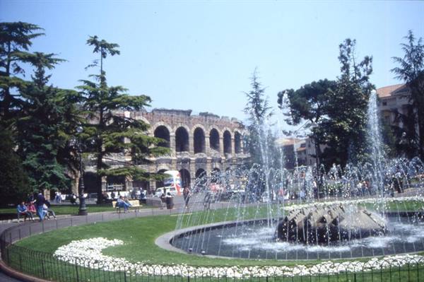 Fountain spraying water in front of Verona Arena, among trees and flowerbeds