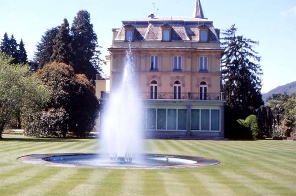 Fountain sprays high water in front of historic villa with green lawn