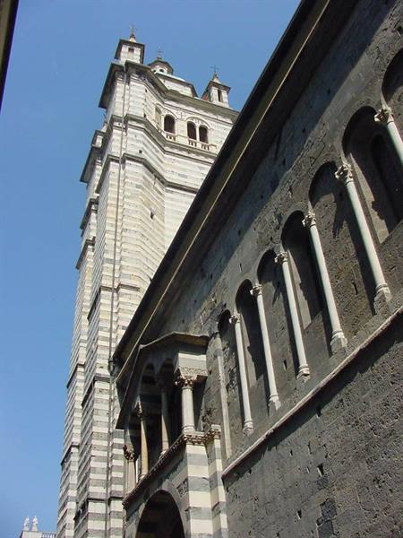 Striped marble bell tower of Genoa Cathedral beside dark stone wall