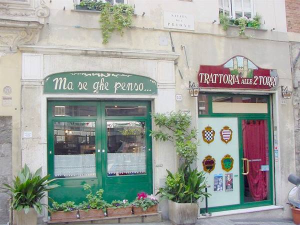 Facade of Trattoria alle 2 Torri, green and red signs, potted flowers