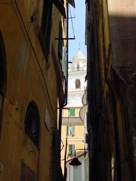 Narrow alley between ochre houses, white bell tower behind, hanging street lamp