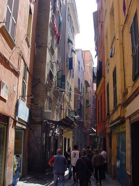 Pedestrians in a narrow alley between tall colorful houses with shutters and hanging laundry