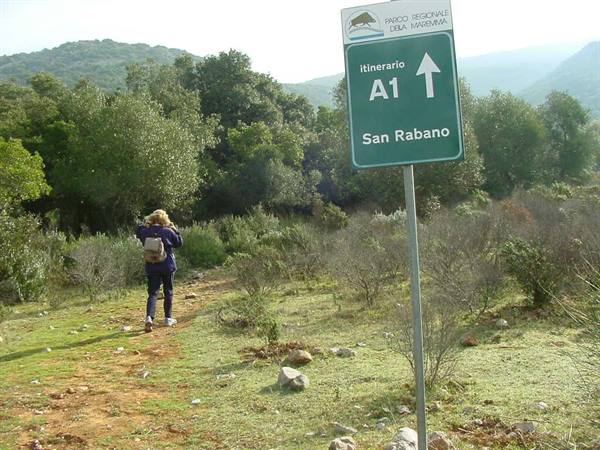 Maremma Park sign for trail A1 to San Rabano, hiker walking uphill