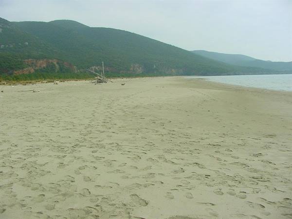 Sandy beach with footprints, a stranded boat and green hills behind