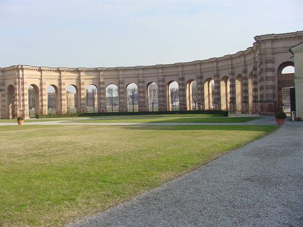 Curved brick arcade with arches, in front of lawn and gravel path