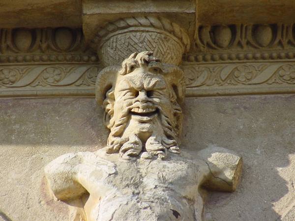 Horned bearded satyr carved in light stone beneath a carved column