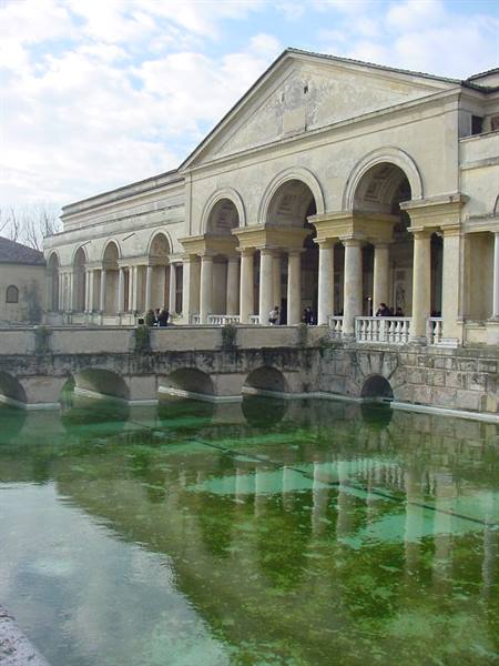 Arched loggia with columns reflected in green water, visitors crossing the stone bridge