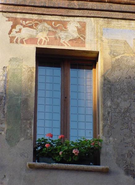 Wooden window with pink geraniums beneath a faded horse fresco