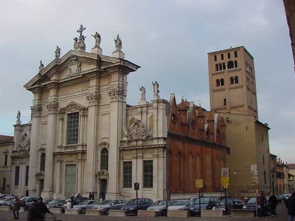 Mantua Cathedral: marble facade and romanesque bell tower, parked cars under grey sky