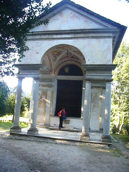 Backpacker examines a frescoed chapel with stone columns among trees