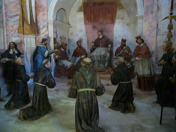 Statues of kneeling friars before the pope and cardinals, pale frescoed walls