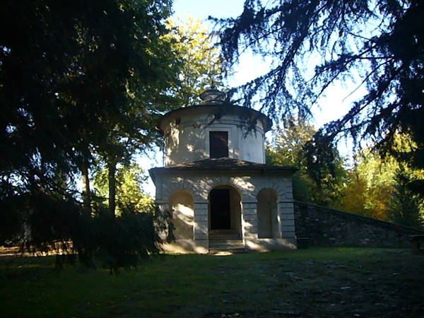 Round stone chapel with arches, among sunlit trees in a park