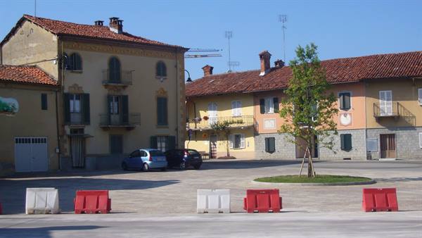 Village square with colorful houses, terracotta roofs, parked cars and red barriers