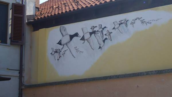 Mural of flying ducks painted on yellow wall beneath tiled roof