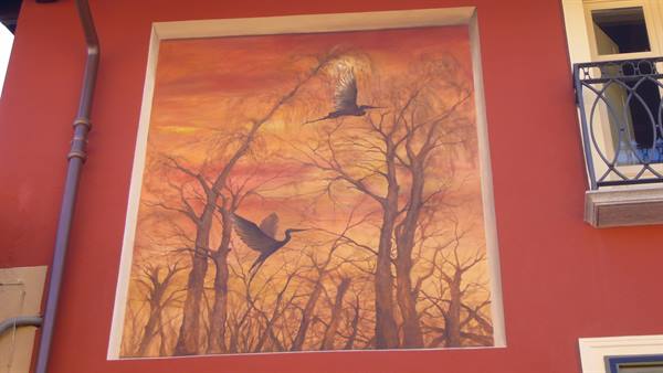 Mural of herons flying among bare branches, painted on orange wall