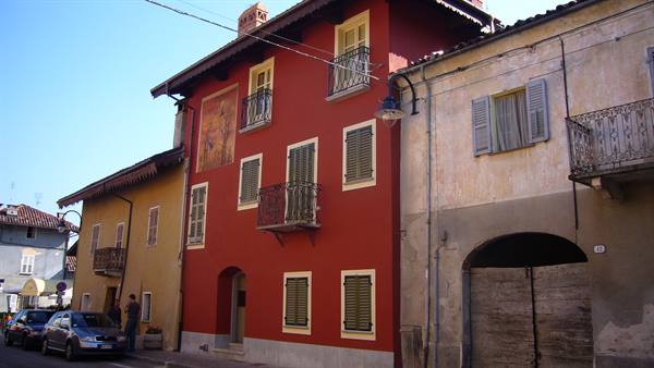 Red house with fresco, iron balconies and green shutters along the street