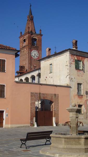 Brick bell tower with clock over square, bench and stone fountain