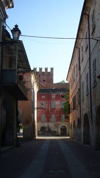 Cobbled street with arcades between old houses and a crenellated tower