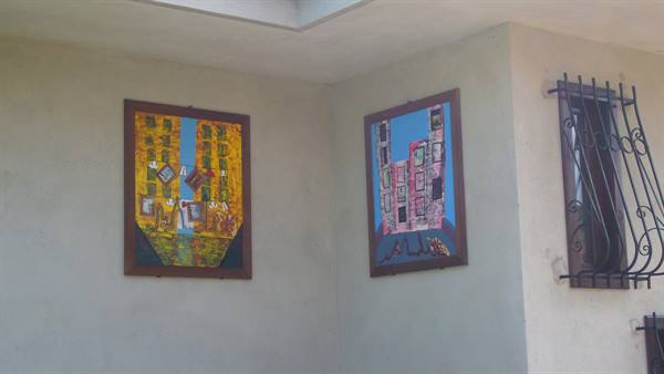 Two wall paintings of colorful buildings on white wall, window with wrought iron grate