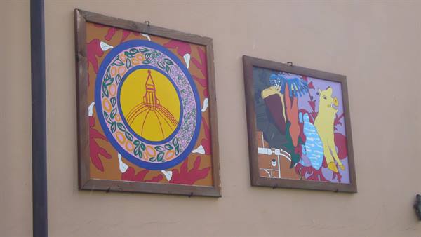 Two colorful paintings hanging on an ochre outdoor wall