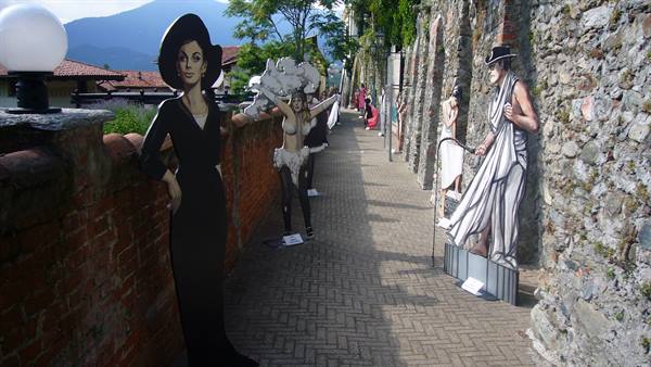 Cutout boards of costumed figures line the stone-walled walkway in Cannero Riviera