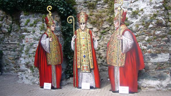 Three life-sized painted bishop cutouts standing against an ivy-covered stone wall
