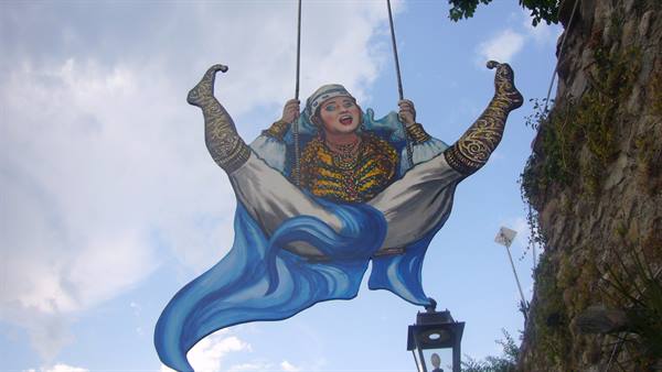 Metal decoration of a floating woman against the sky, near a stone wall