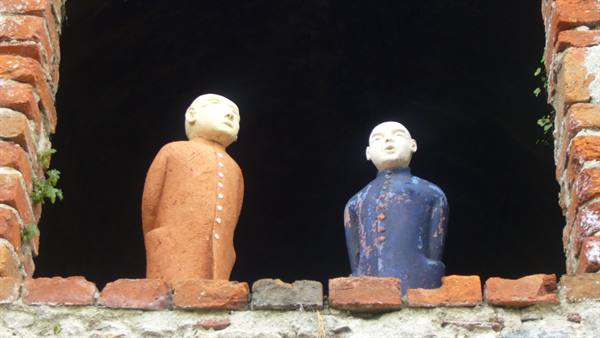 Two ceramic statues on brick wall, inside a dark opening