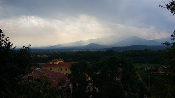 Red rooftops among trees, misty mountains under a cloudy sky