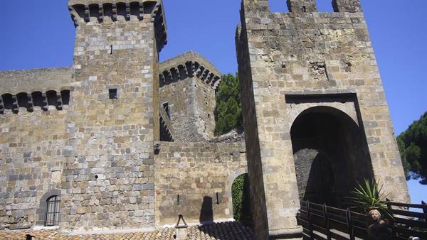 Medieval stone towers with machicolations and arched gateway under blue sky