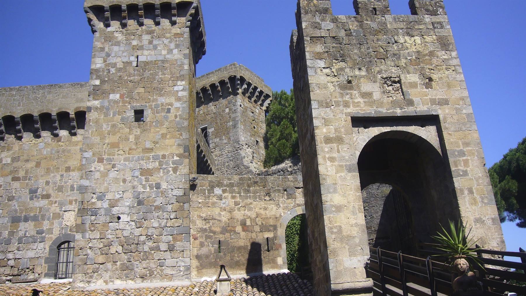 Torri medievali in pietra con beccatelli e portale ad arco sotto cielo blu