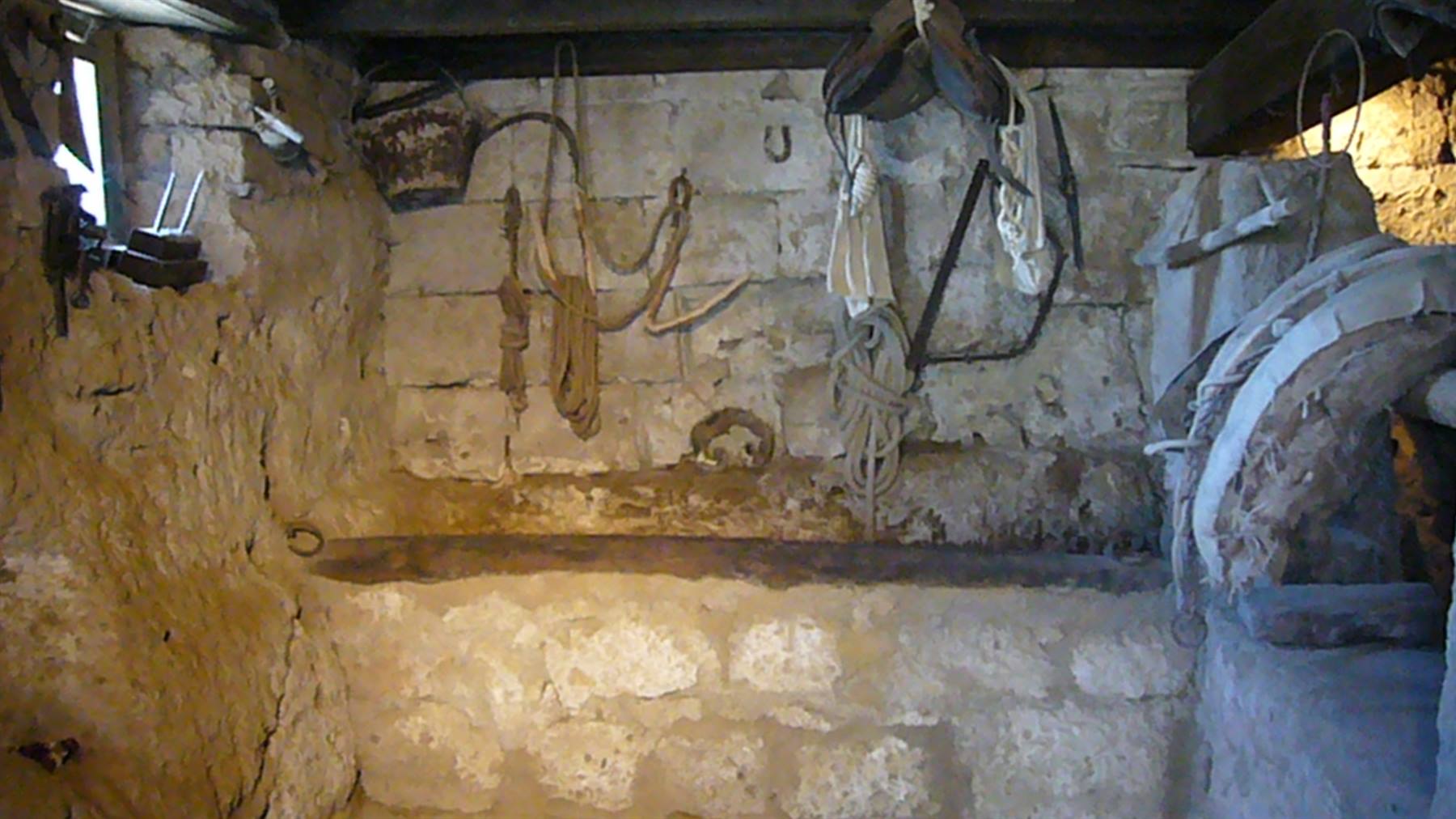 Stalla rustica con muri di pietra, corde e attrezzi agricoli appesi