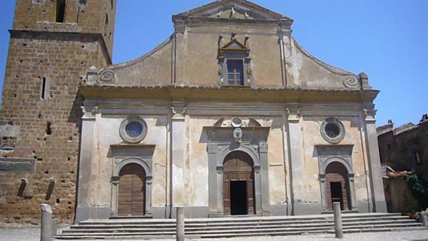 Ochre baroque church facade with stone bell tower and steps under blue sky