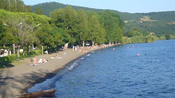 Sandy beach on Lake Bolsena, sunbathers on the shore and swimmers in blue water