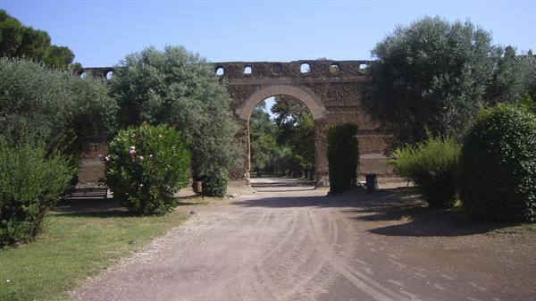 Brick archway of an ancient city wall, dirt path among oleanders and pines, sunlight