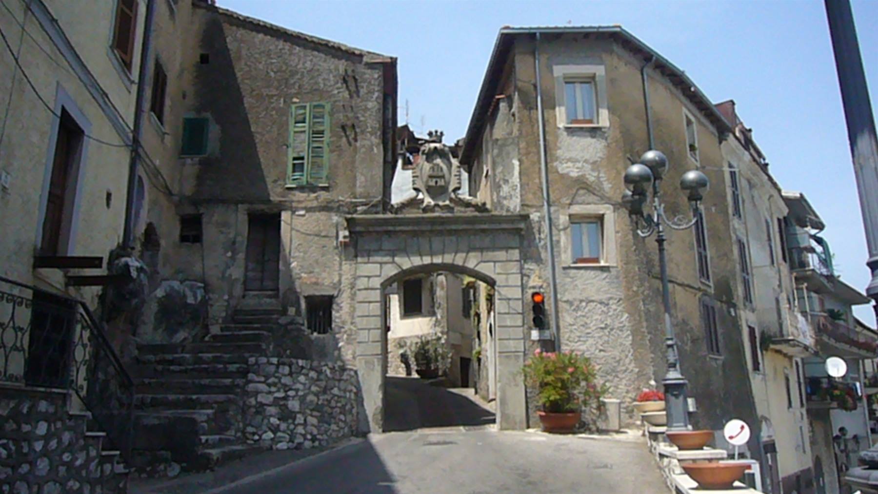 Porta medievale in pietra tra vecchi caseggiati, scalinata e lampione a destra