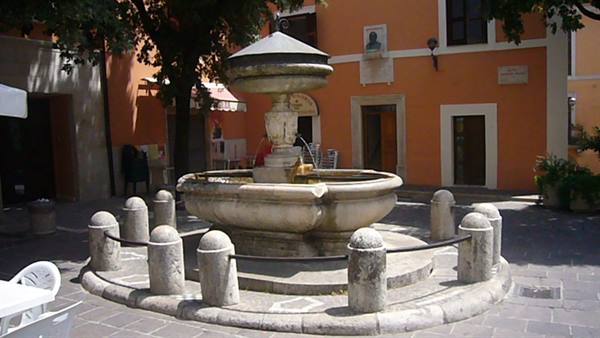 Stone fountain surrounded by bollards in a square with ochre buildings