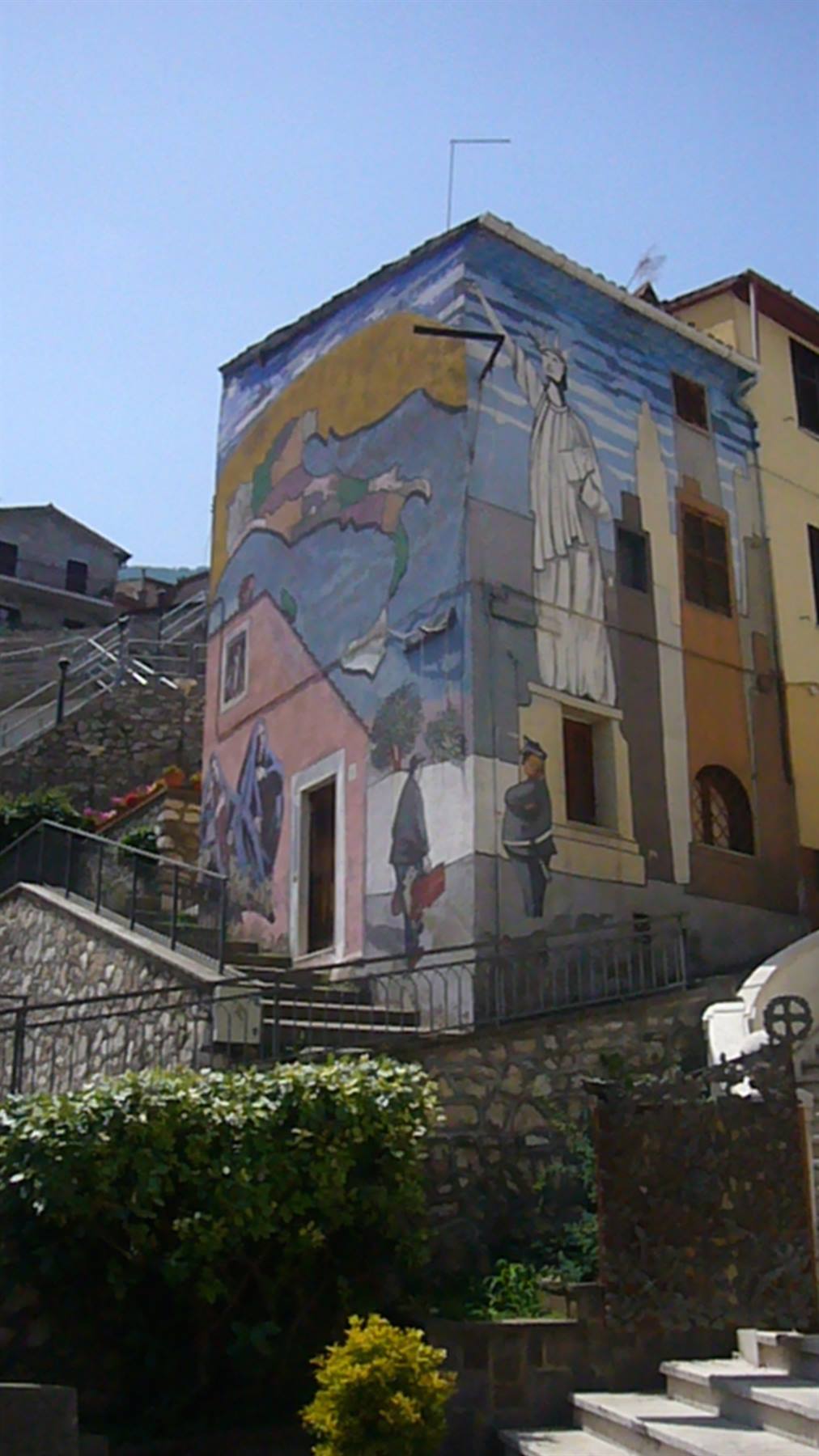Casa dipinta con un grande murales colorato, scalinate in pietra sotto cielo azzurro
