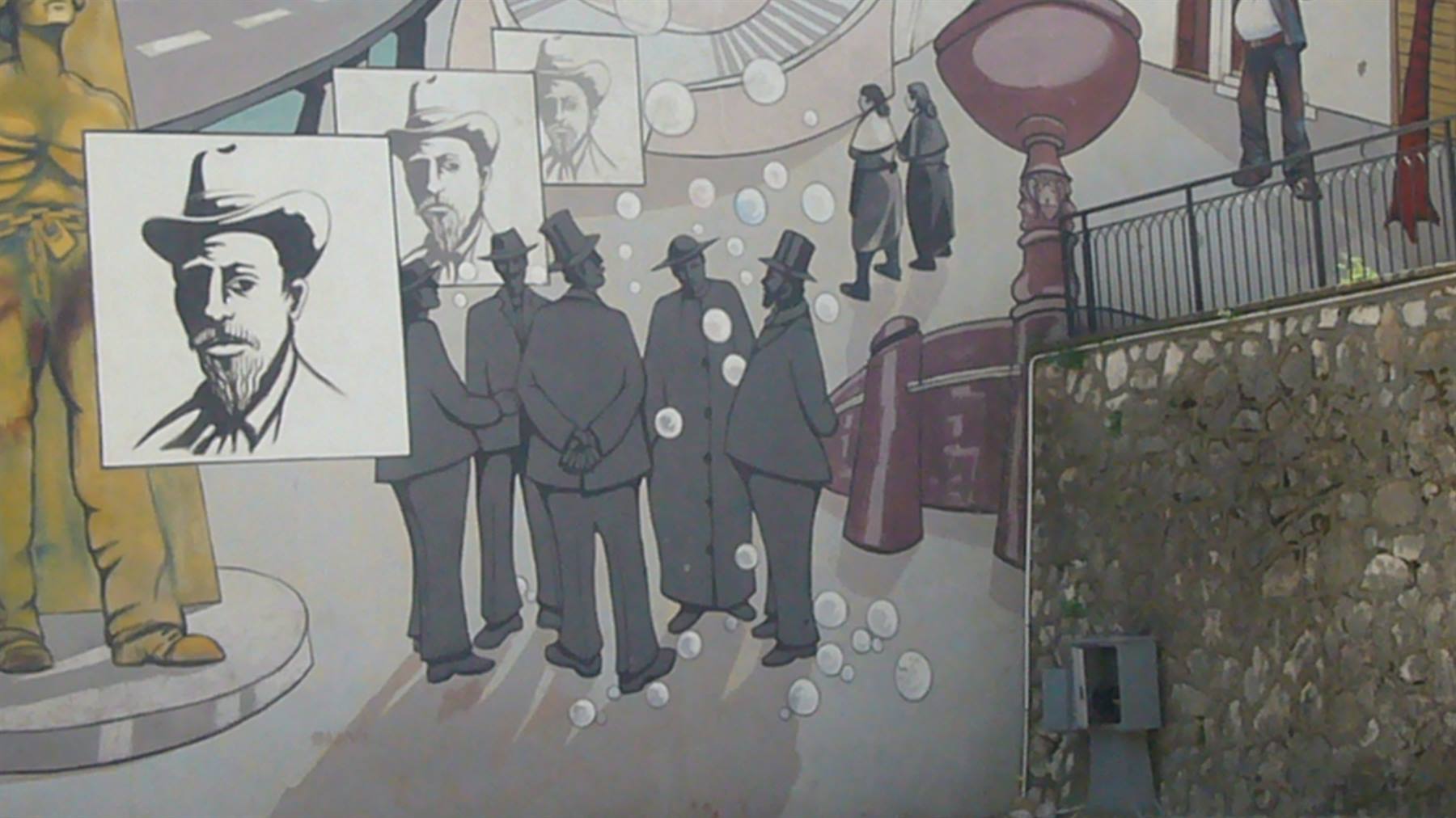 Murale con uomini in cappello e ritratti monocromatici accanto a muro di pietra