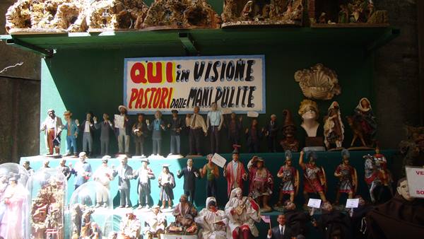 Nativity figurines displayed on green counter, anticorruption sign, Naples workshop