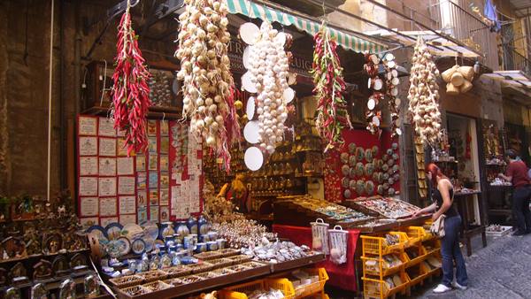 Street market with hanging garlic braids and red peppers, tourist browsing the stalls