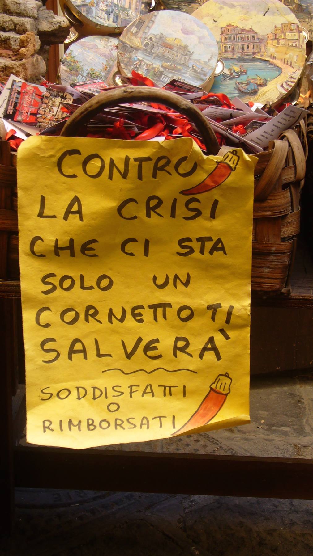 Cartello giallo scritto a mano contro la crisi, cesto di souvenirs dipinti
