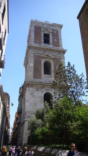 Renaissance marble and brick bell tower in Naples, tourists below in sunlight