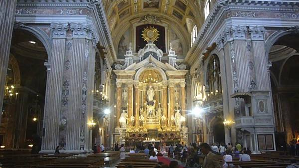 Inside Genoa's San Lorenzo Cathedral, baroque altar and visitors among striped marble columns