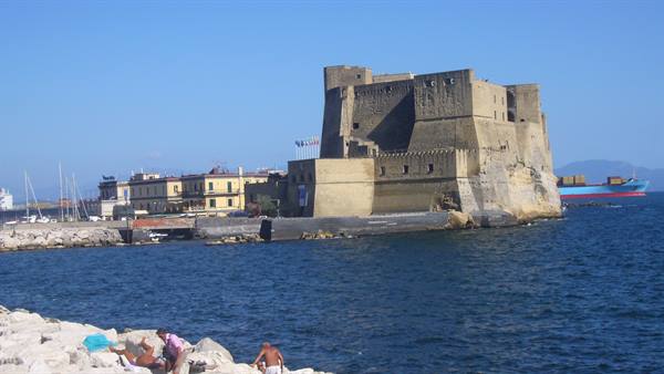Castel dell'Ovo in Naples, tourists on the rocks under blue sky