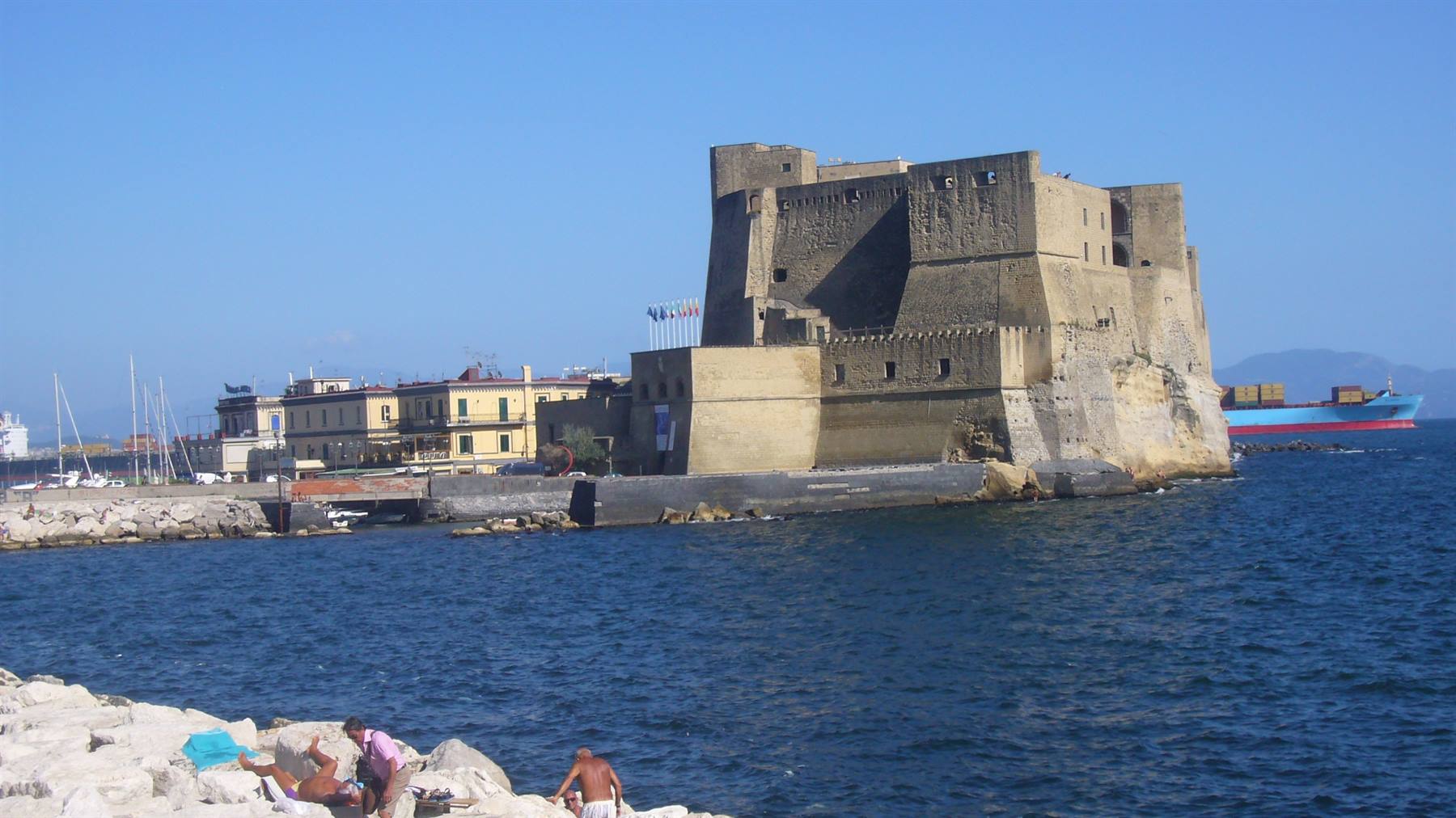 Castel dell'Ovo a Napoli, turisti sulla scogliera sotto il cielo azzurro