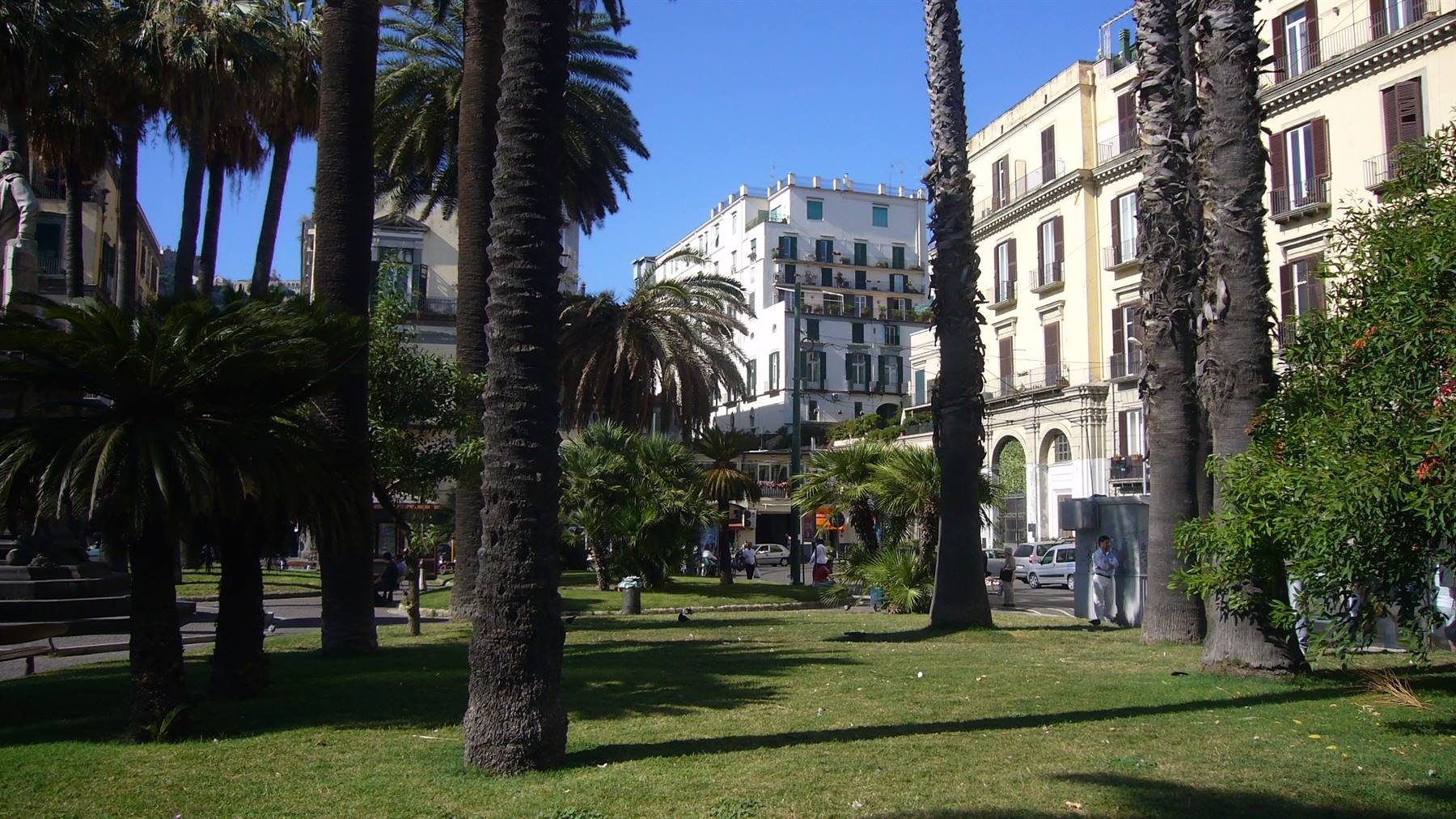 Palme e edifici nel parco della Villa Comunale a Napoli, luce intensa